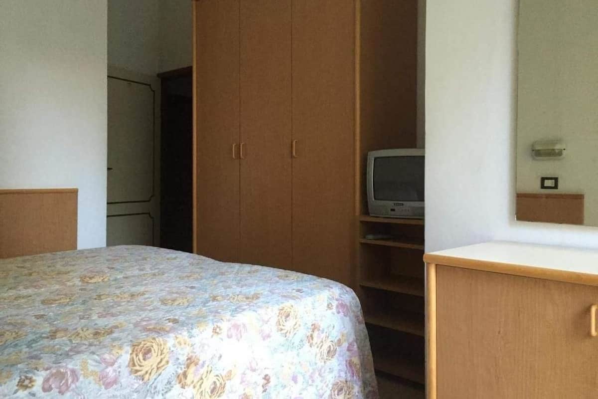 A bedroom with a bed, a wooden wardrobe, and a television on a shelf.