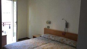 Ein Hotelzimmer mit einem Bett, einem Nachttisch, einem an der Wand befestigten Telefon und einem Fenster mit Ausblick.