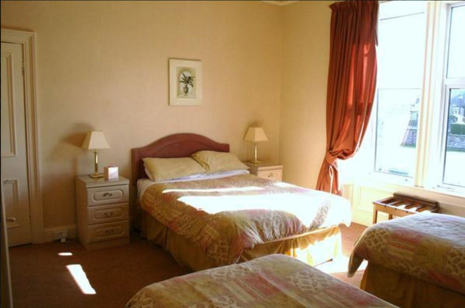 Un dormitorio con dos camas, una mesita de noche con lámpara, un aparador y una ventana con cortinas.