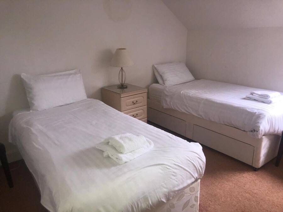Quarto duplo com duas camas, uma mesinha de cabeceira e uma luminária.