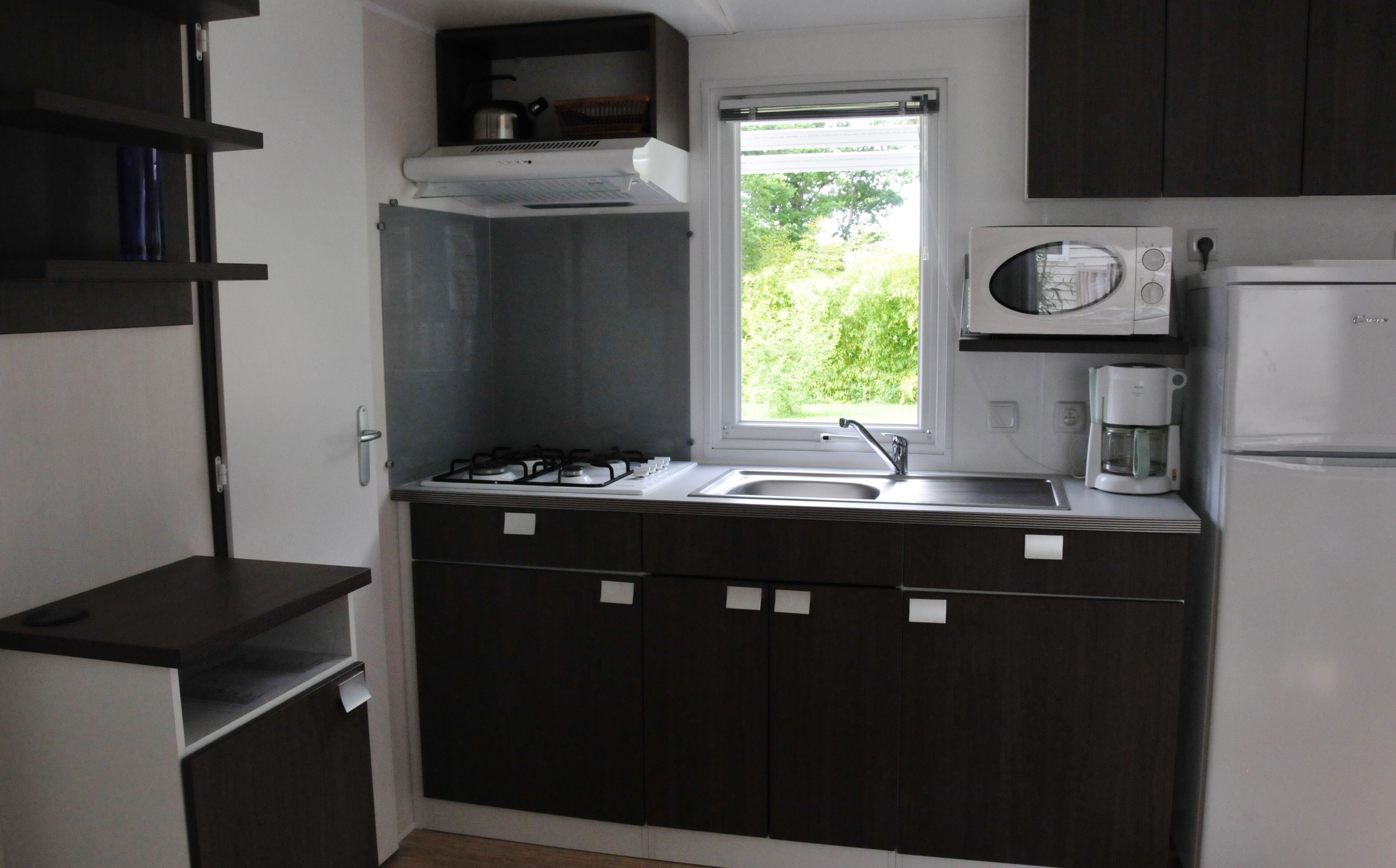 Una cocina compacta con muebles oscuros, estufa a gas, microondas y refrigerador.