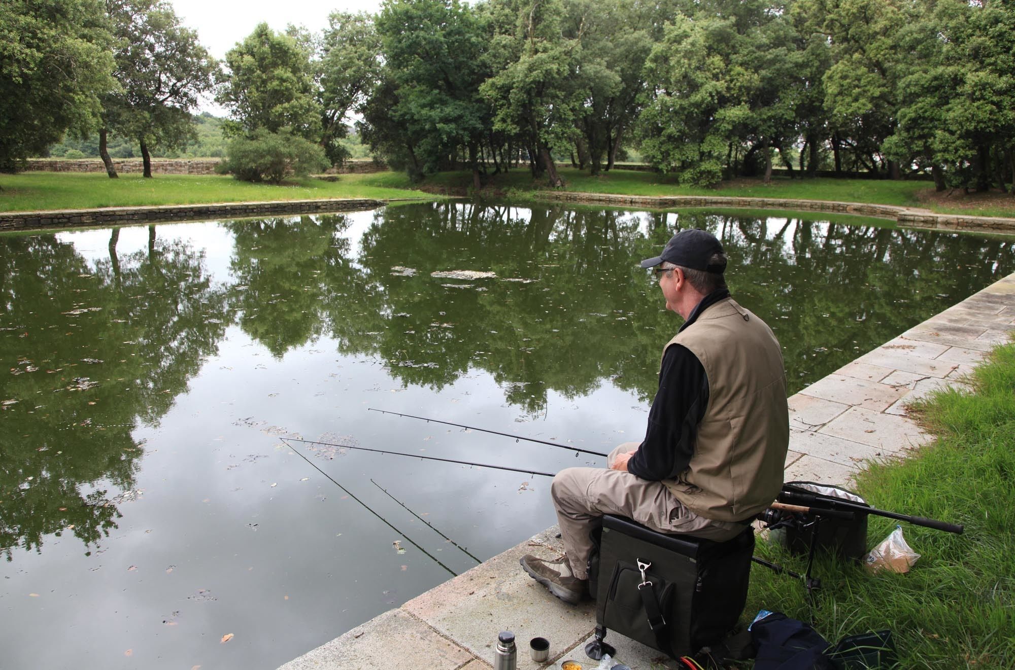 Un hombre sentado junto a un estanque tranquilo pescando.