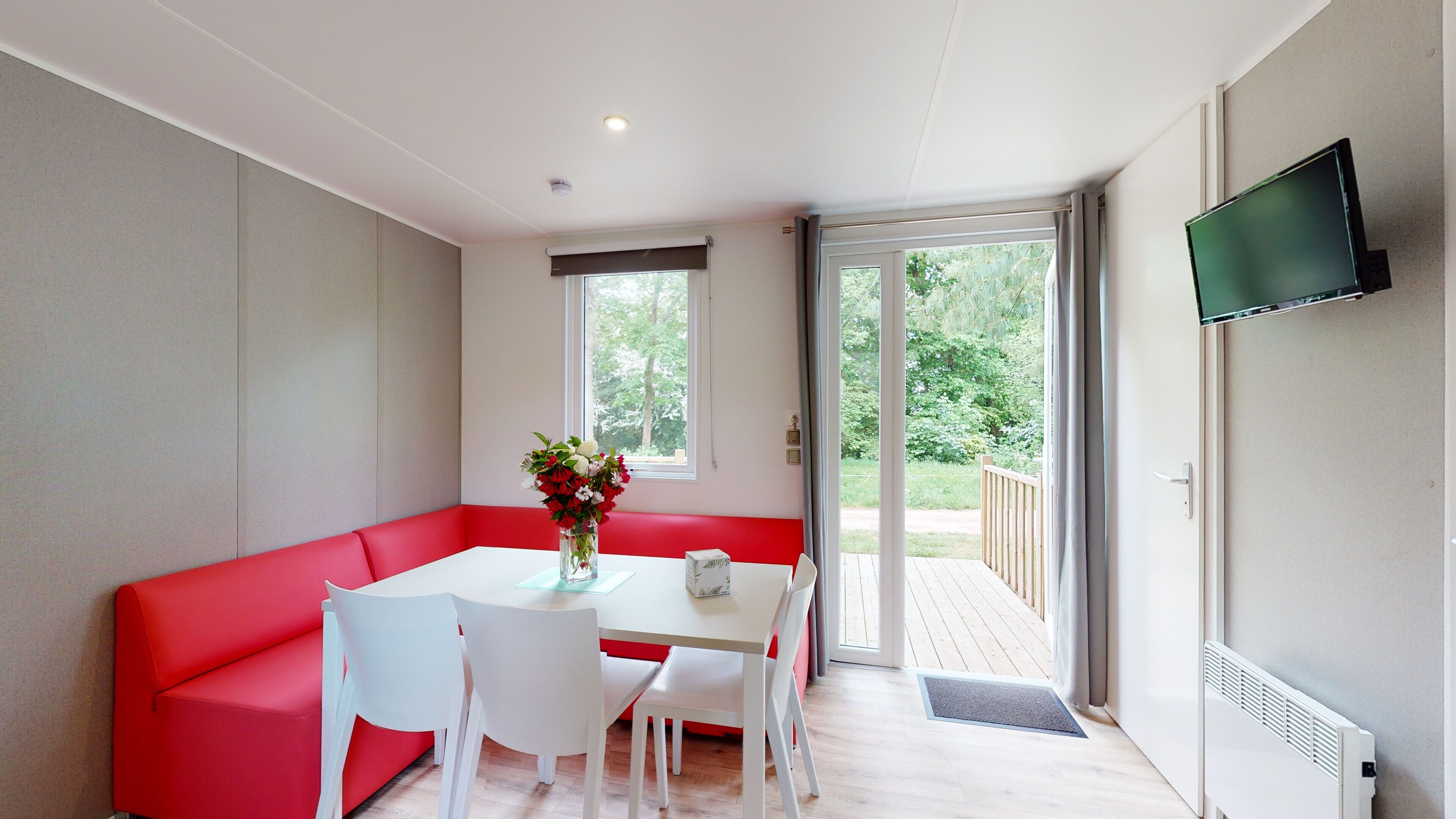A modern room with a red sofa, white chairs, a small table with a vase of flowers, and a TV on the wall.