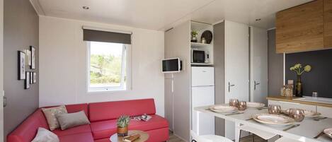 A compact living space with a red sofa, a small round table, a white dining table with chairs, a microwave, and a wooden cabinet.
