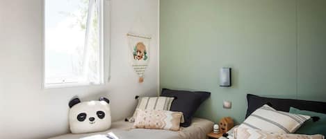 Une chambre avec deux lits simples, une fenêtre avec un store, une lampe fixée au mur et une décoration murale.