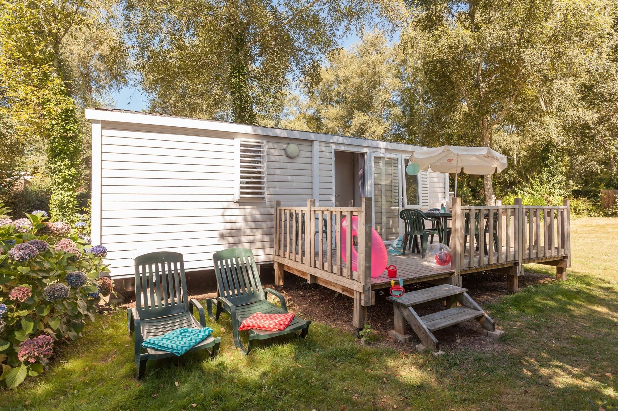 A mobile home with a deck, outdoor seating, and a garden with hydrangeas.
