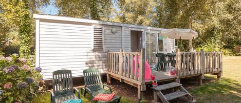 A mobile home with a deck, outdoor seating, and a garden with hydrangeas.