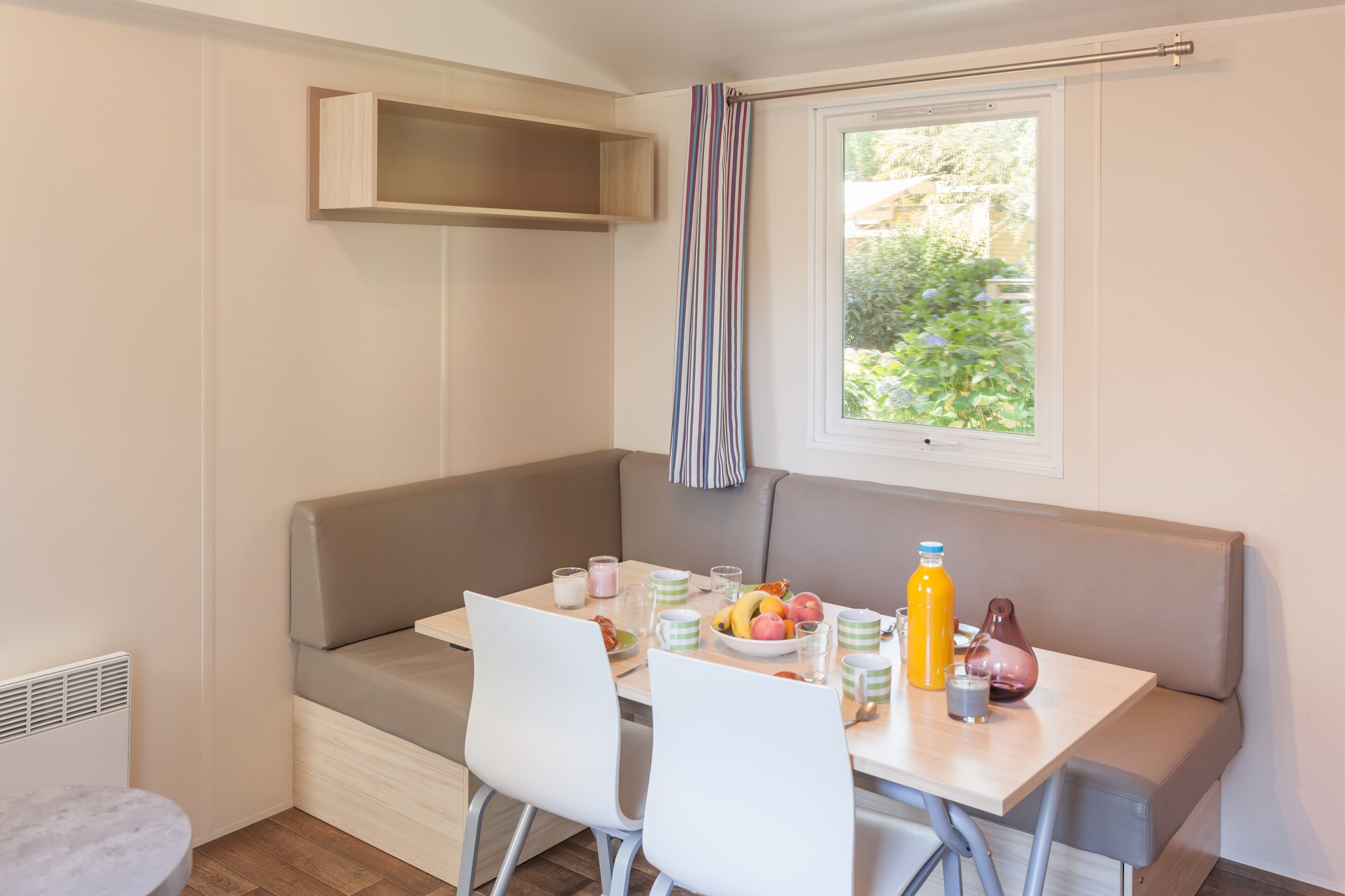 A breakfast nook with a bench, a table, and chairs. There is a window with a view of greenery outside.