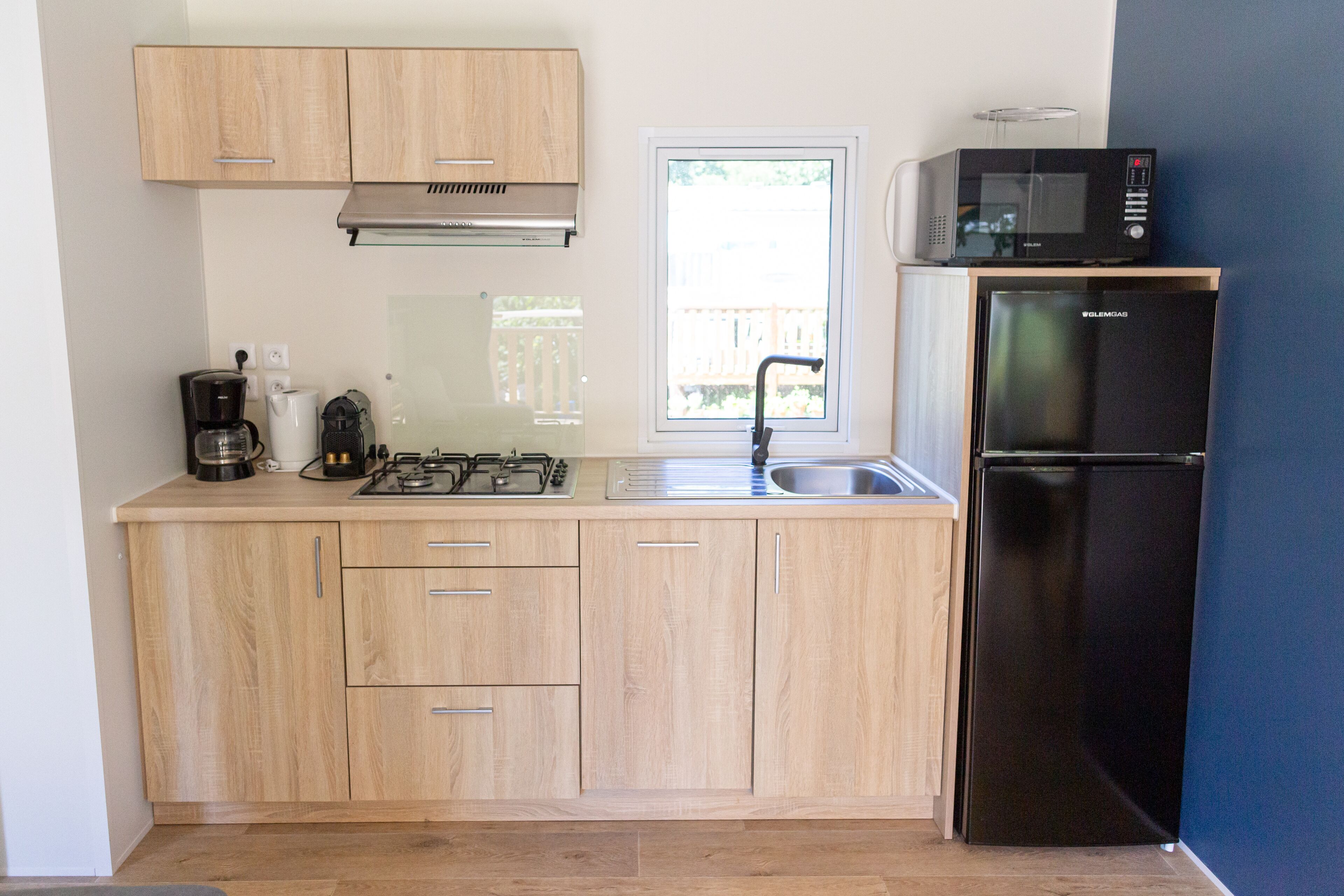 A kitchen with wooden cabinets, a gas stove, a coffee maker, a microwave, and a refrigerator.