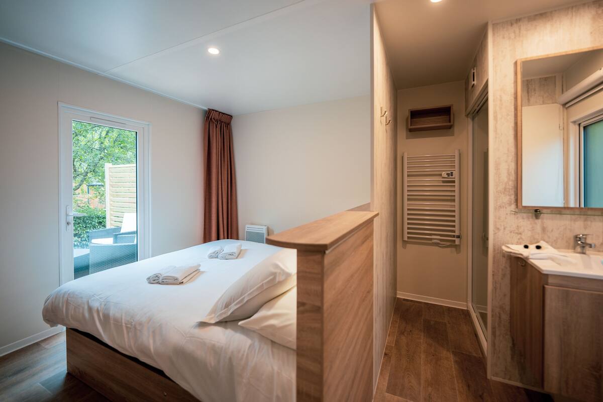 Un dormitorio con cama, un baño con lavamanos y espejo, y una ventana con cortinas.