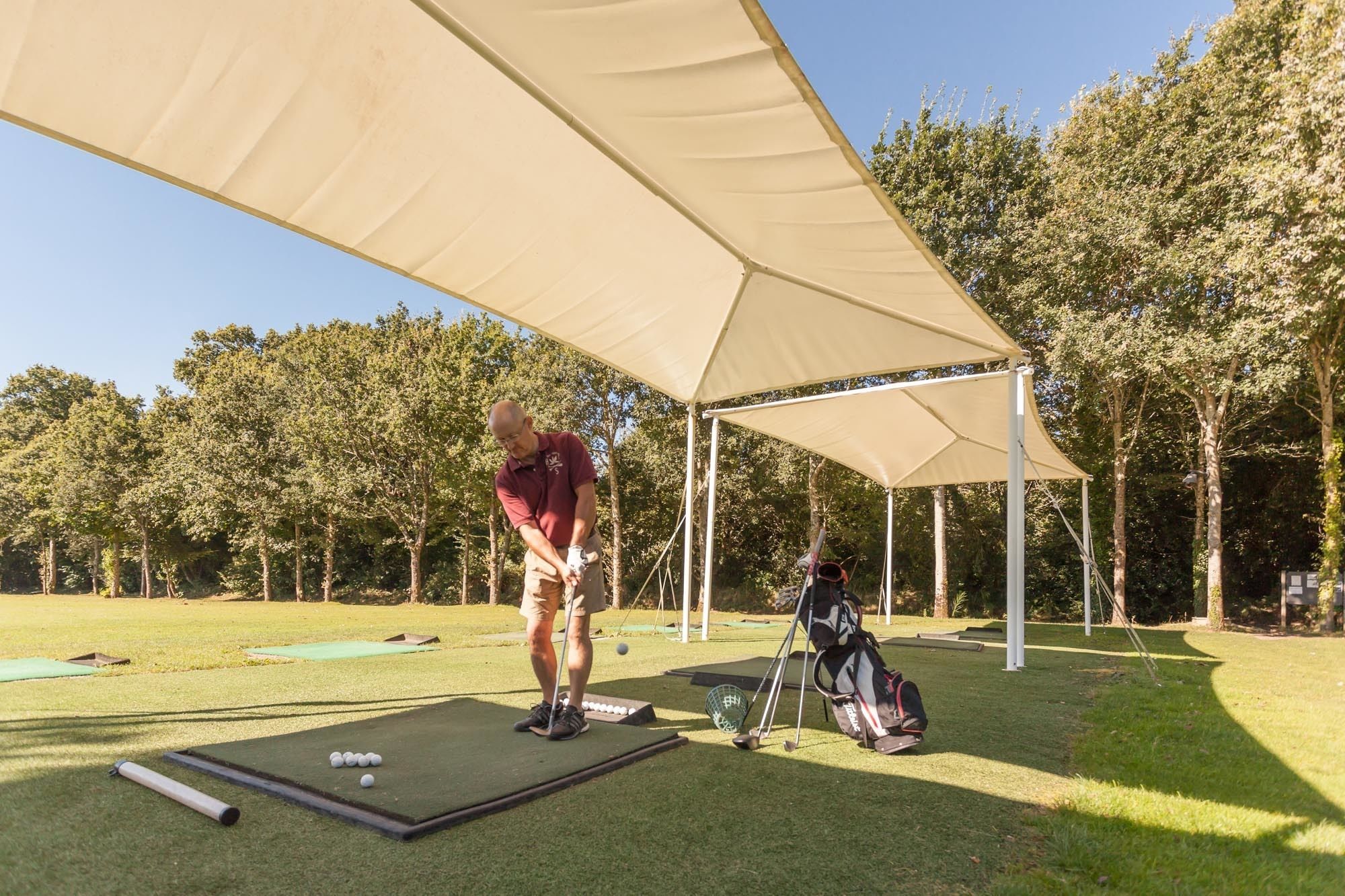 A golf practice area with a canopy, putting mats, and a bag of golf balls.
