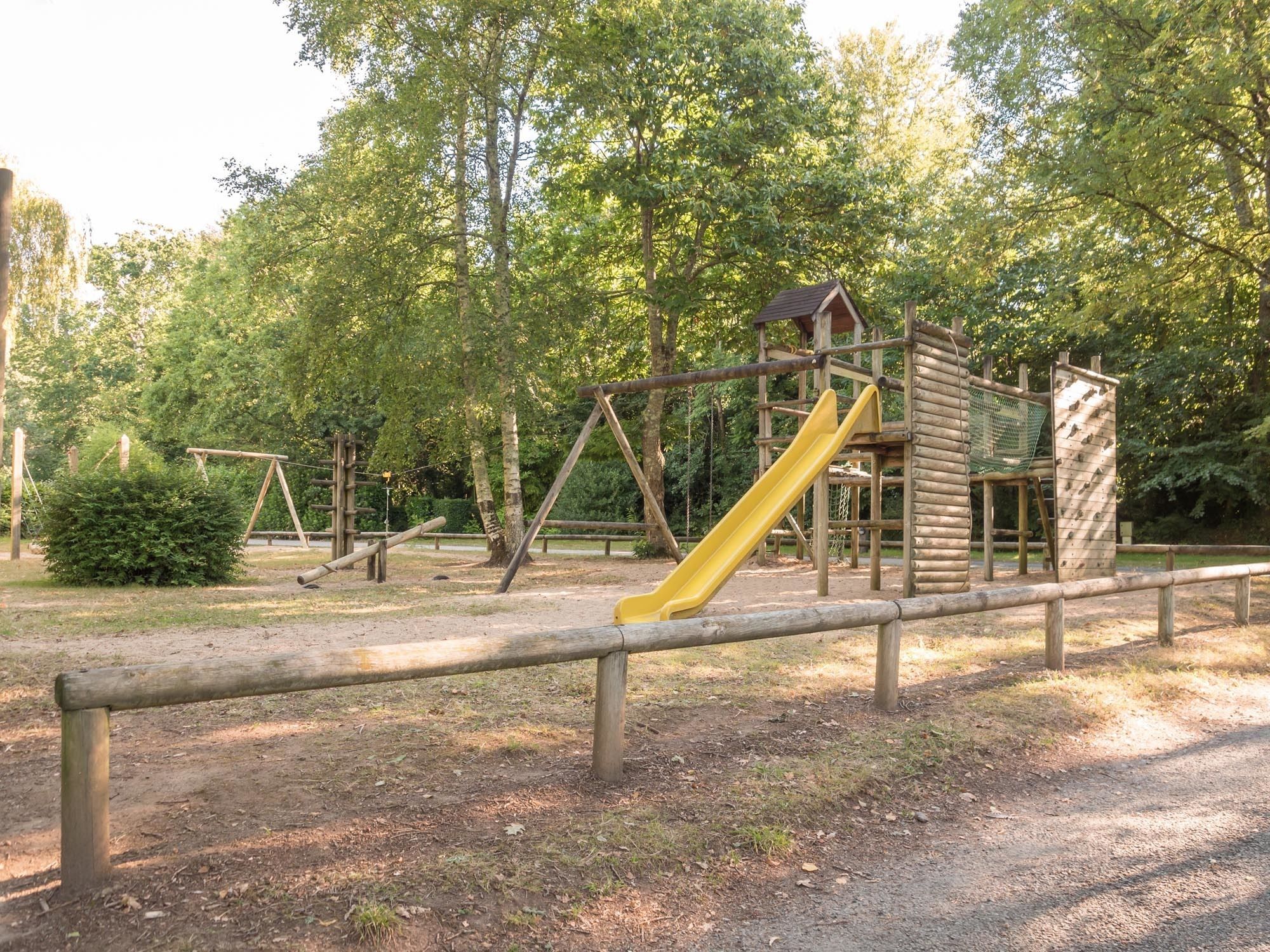 A playground with a slide and climbing structures, surrounded by trees.