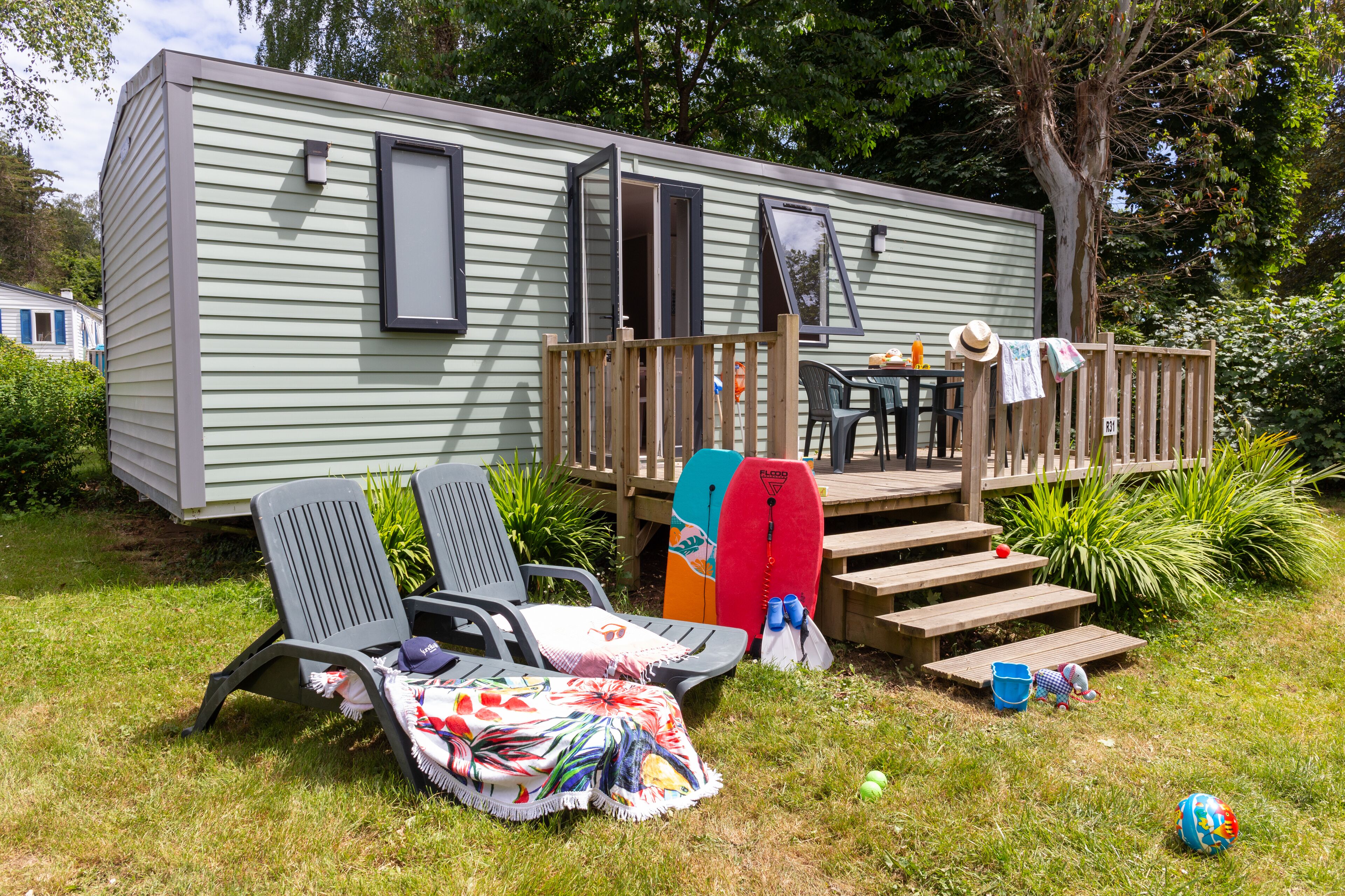 A mobile home with a deck, two lawn chairs, a beach towel, and a surfboard.