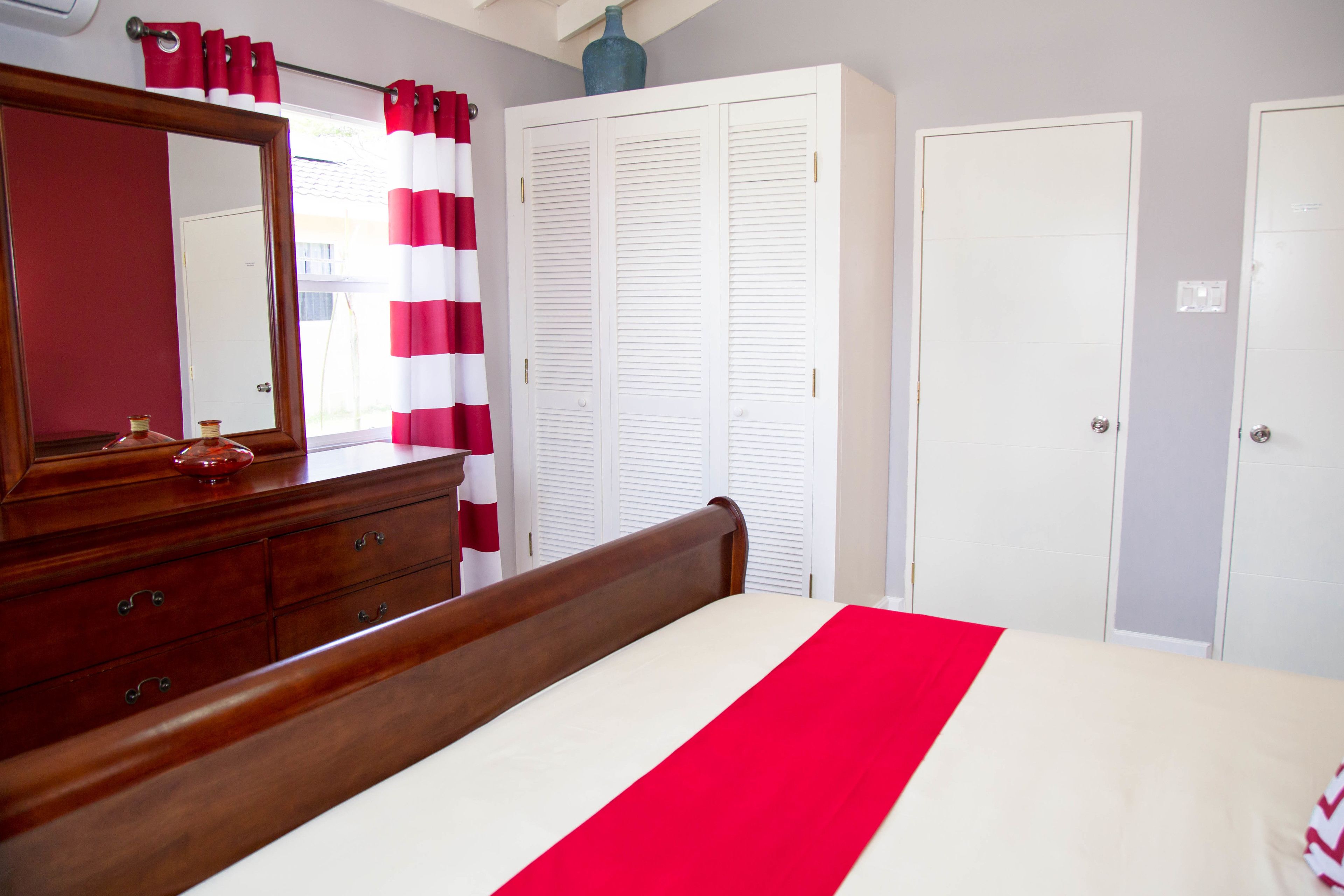 Een slaapkamer met een houten bed, een dressoir, een spiegel, een kledingkast en een douchegordijn.