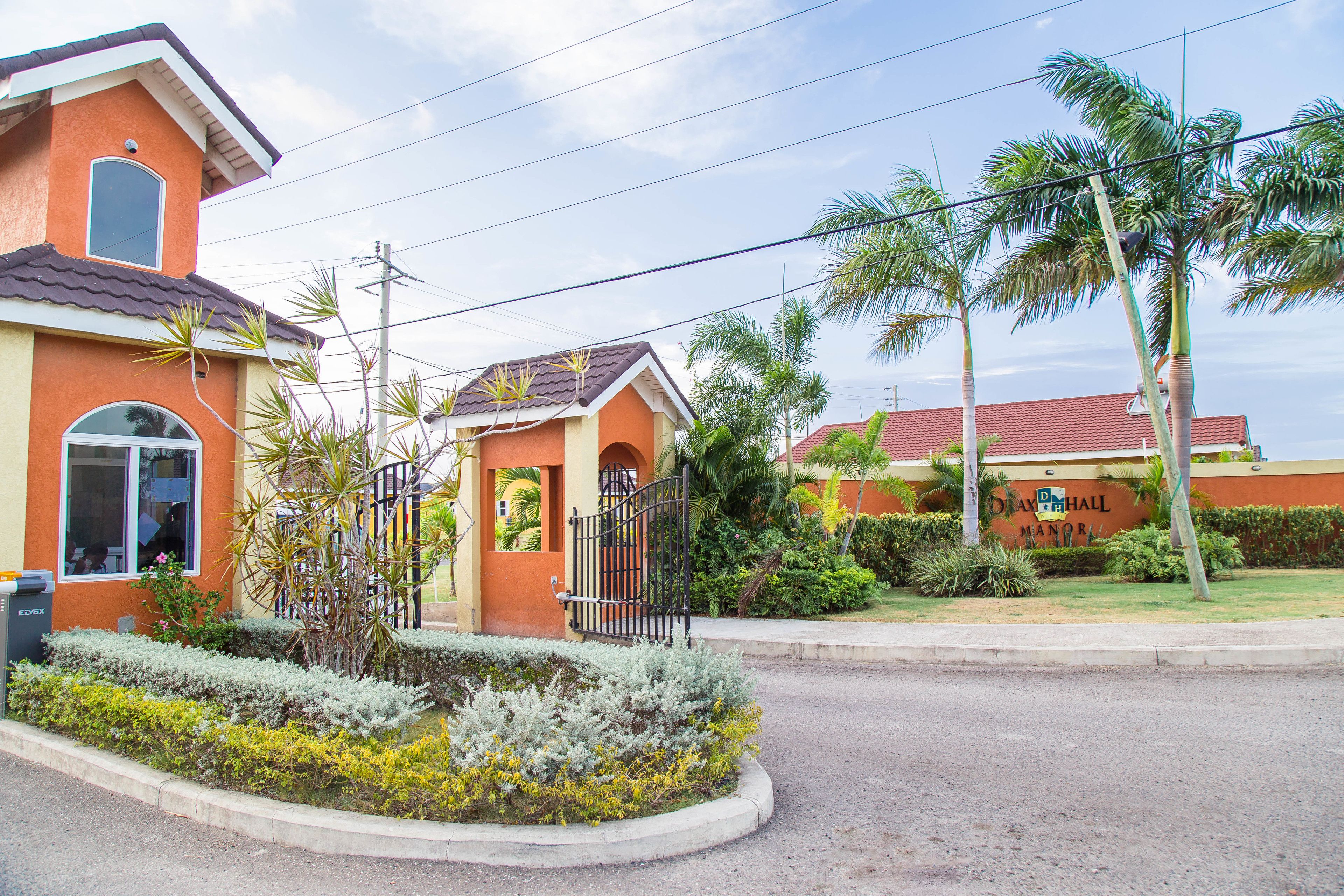 A residential area with a house featuring a red roof, a gated entrance, and a well-maintained garden with various plants.
