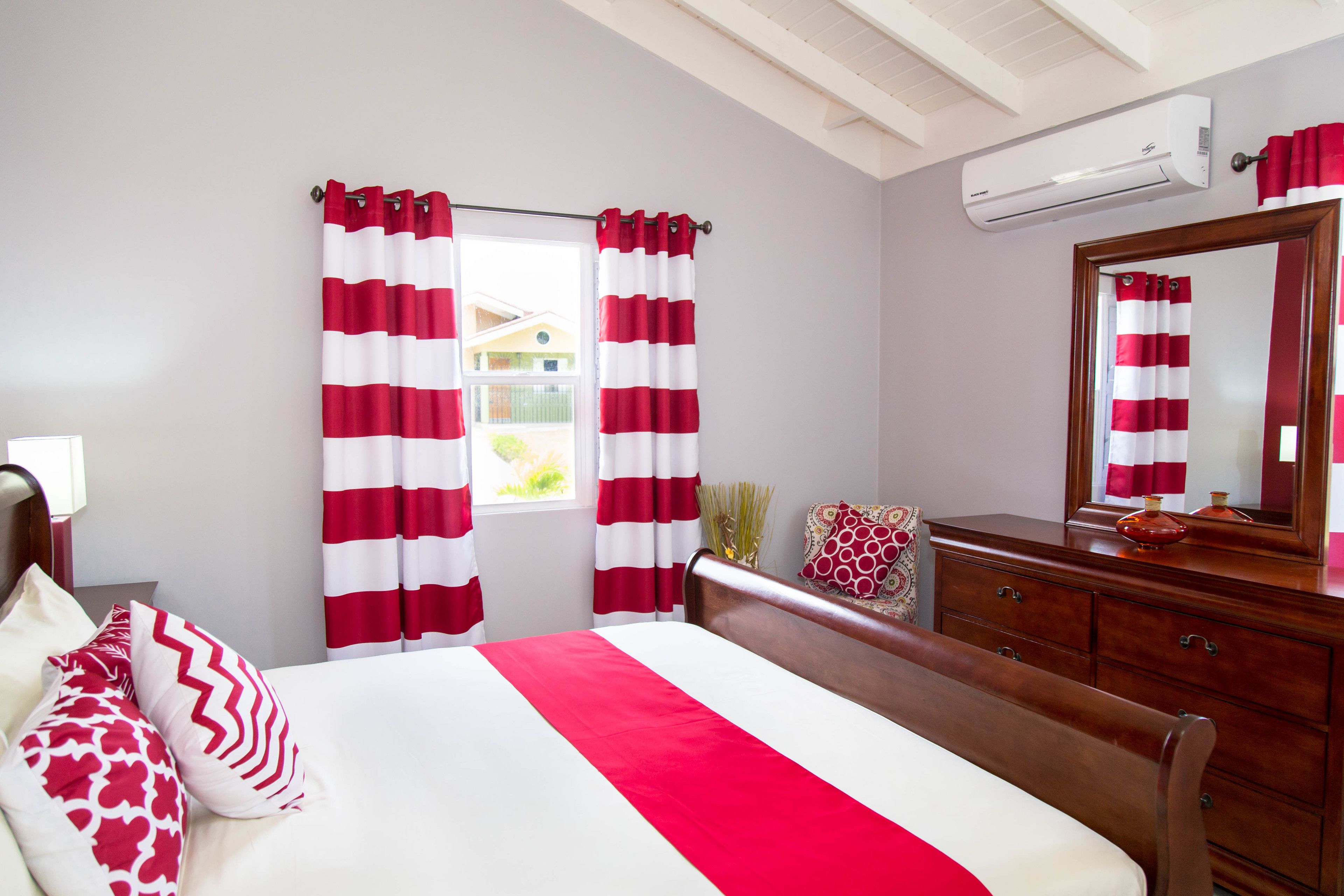 A hotel room with a bed, a dresser, a mirror, and red and white striped curtains.