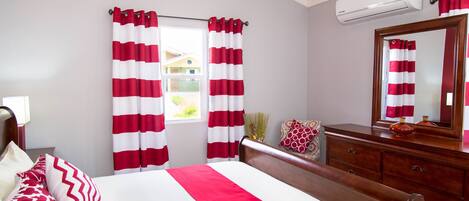 A hotel room with a bed, a dresser, a mirror, and red and white striped curtains.