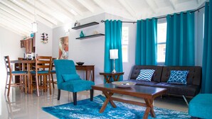 Un salon moderne avec un canapé, un fauteuil turquoise, une table basse en bois et un coin repas comprenant une table et des chaises en bois.