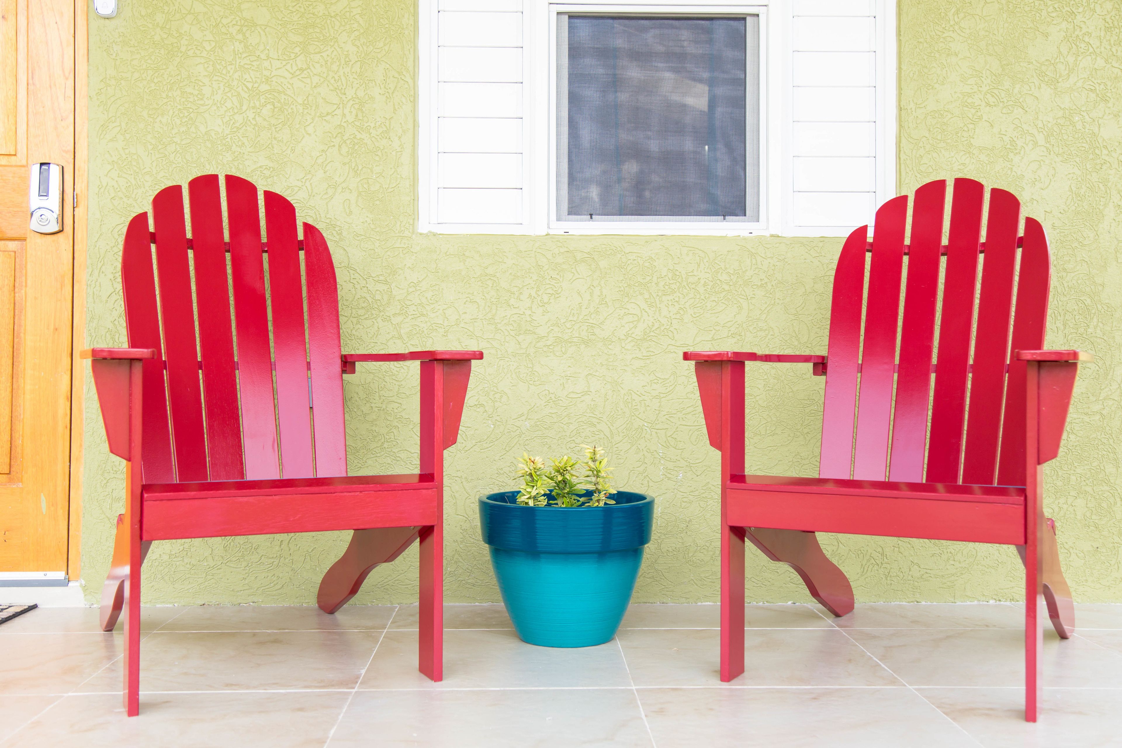 Two red Adirondack chairs with a blue planter between them.