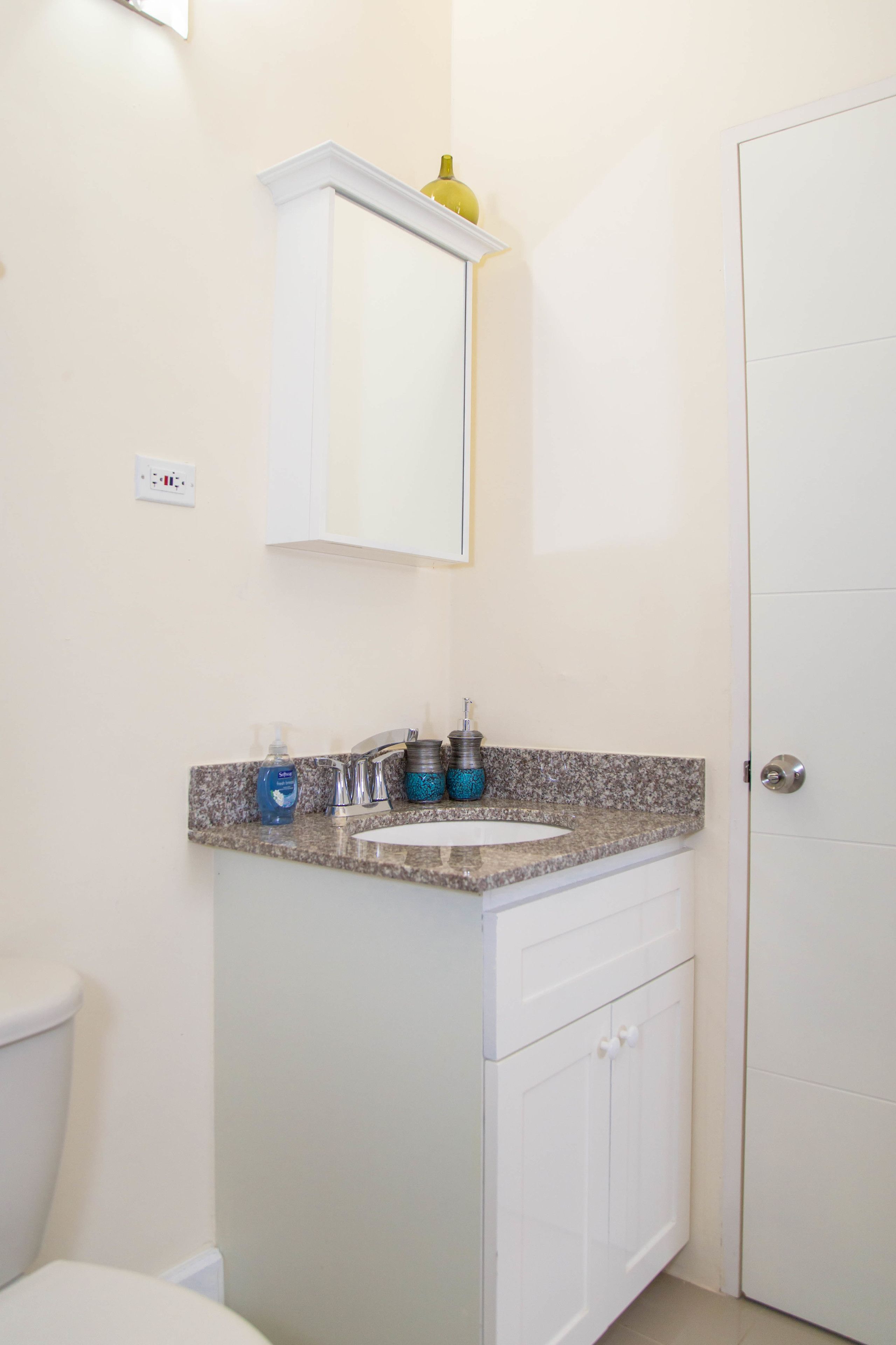 A bathroom with a white toilet, a granite countertop sink, a mirror above the sink, and a white door.