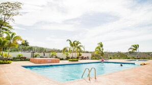 Une piscine dotée d’une terrasse carrelée, entourée de palmiers et avec des maisons en arrière-plan.