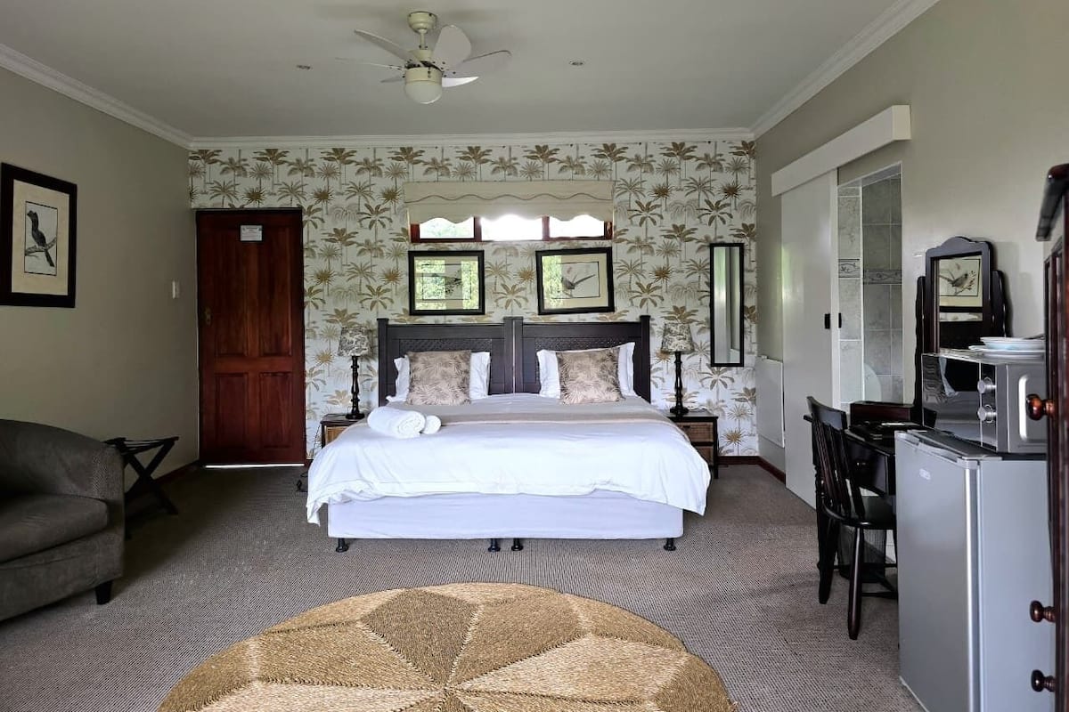 A bedroom with a bed, a desk, a chair, a ceiling fan, and a door.