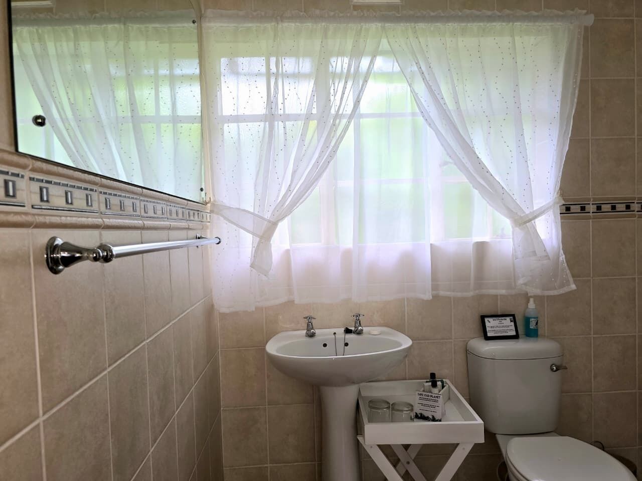 A bathroom with a toilet, sink, and window with sheer curtains.