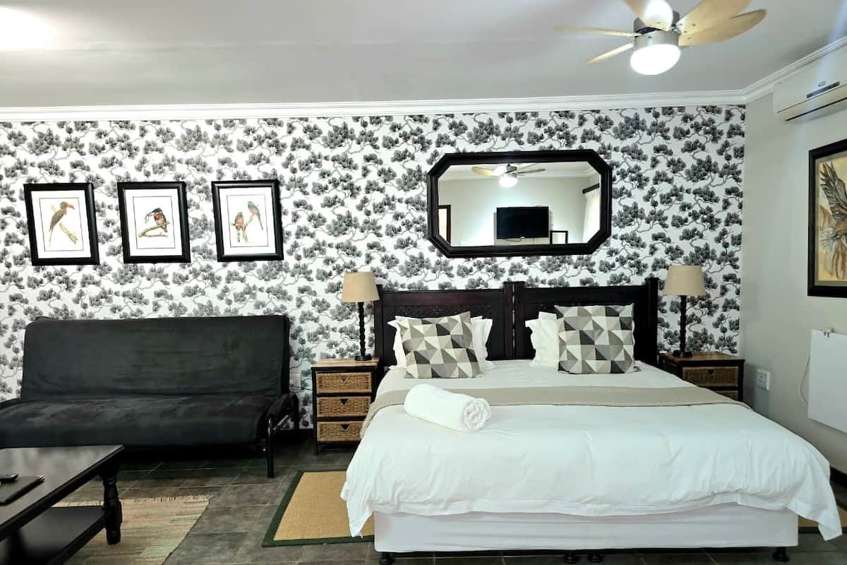 A bedroom with a bed, a sofa, a nightstand, a mirror, and framed pictures on the wall.