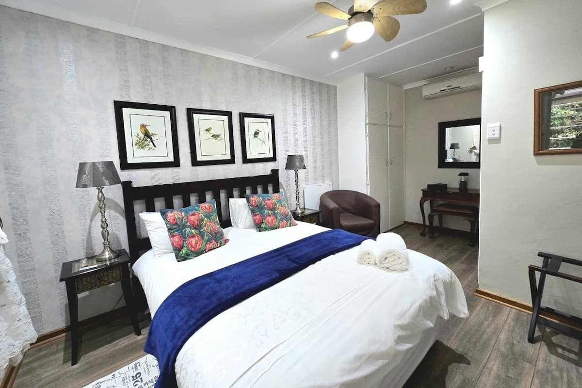 A neatly arranged bedroom with a bed, pillows, a nightstand, a chair, a desk, and a ceiling fan.