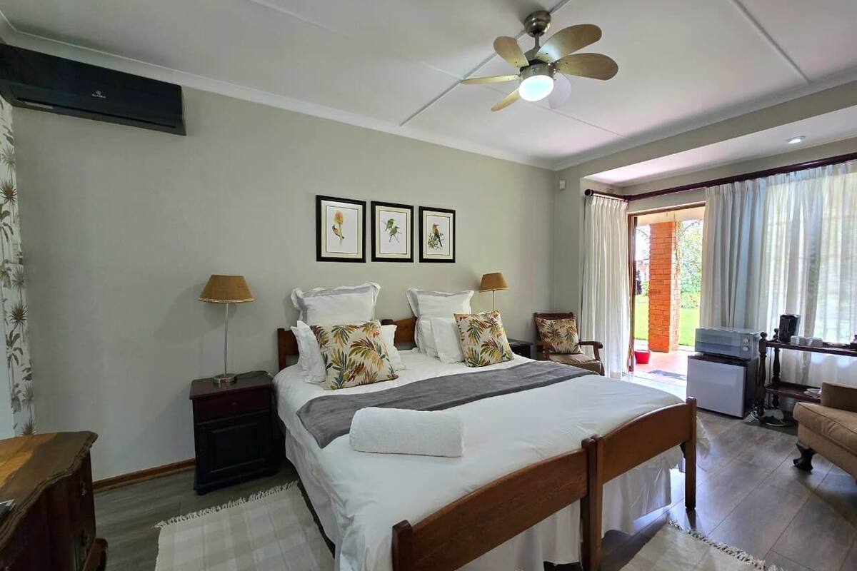 A bedroom with a bed, bedside tables, a ceiling fan, and a view of the outdoors.