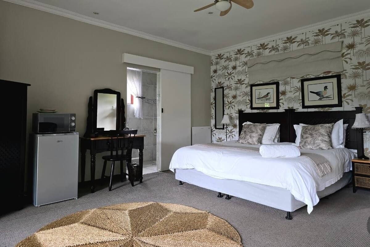 A bedroom with a bed, a desk, a refrigerator, a ceiling fan, and a wall with framed pictures.