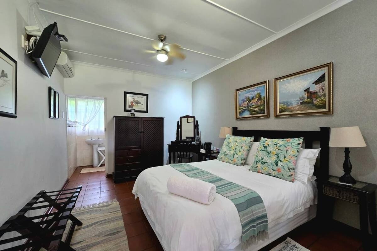 A bedroom with a bed, a desk, a chair, a wardrobe, a television, and two paintings on the wall.