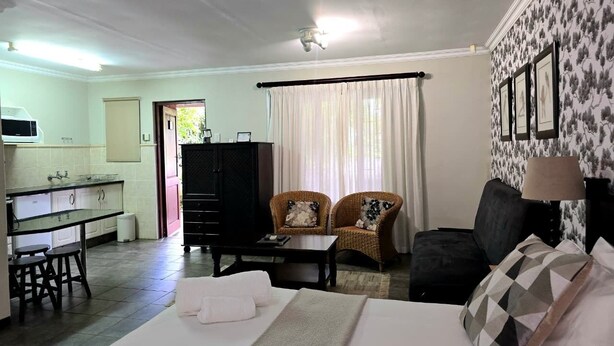 A hotel room with a bed, a dining table, a kitchen area, and a living area with a sofa and chairs. - Birds of paradise B&B (Eshowe)