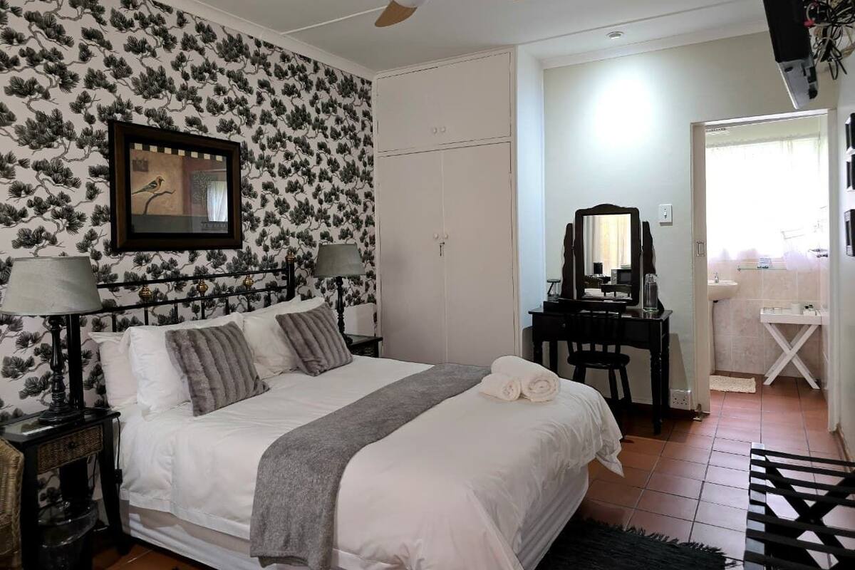 A bedroom with a bed, a desk, a chair, a ceiling fan, and a bathroom visible through an open door.