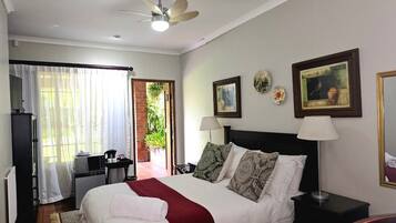 A bedroom with a bed, a desk, a chair, a TV, a ceiling fan, and a door leading to a balcony.