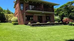 A two-story brick house with a balcony, surrounded by a well-maintained lawn and various shrubs. - Birds of paradise B&B (Eshowe)