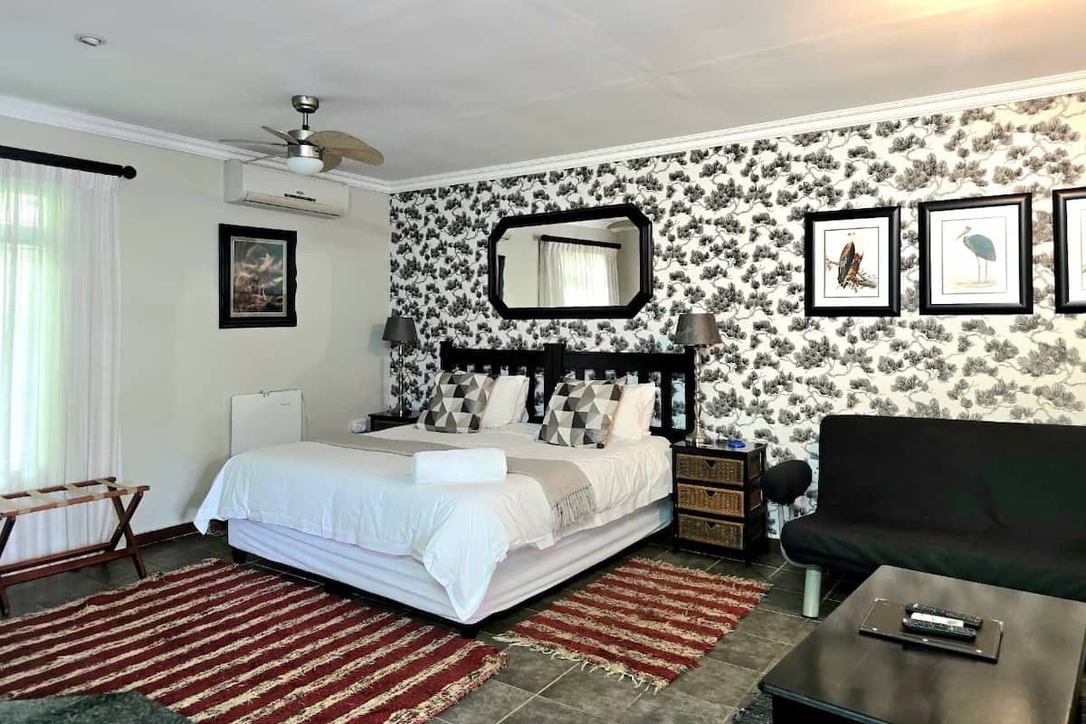 A bedroom with a bed, a nightstand, a dresser, a black sofa, a mirror, and framed pictures on the wall.