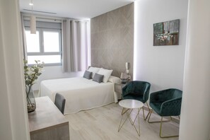A modern hotel room with a large bed, two green armchairs, a small round table, and a painting on the wall. - Énfasis Hotel (El Cuervo de Sevilla)