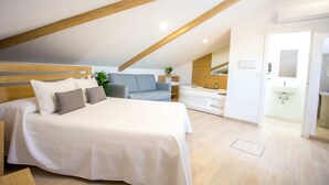 A modern bedroom with a large bed, a sofa, a bathtub, and a bathroom with a sink and mirror.