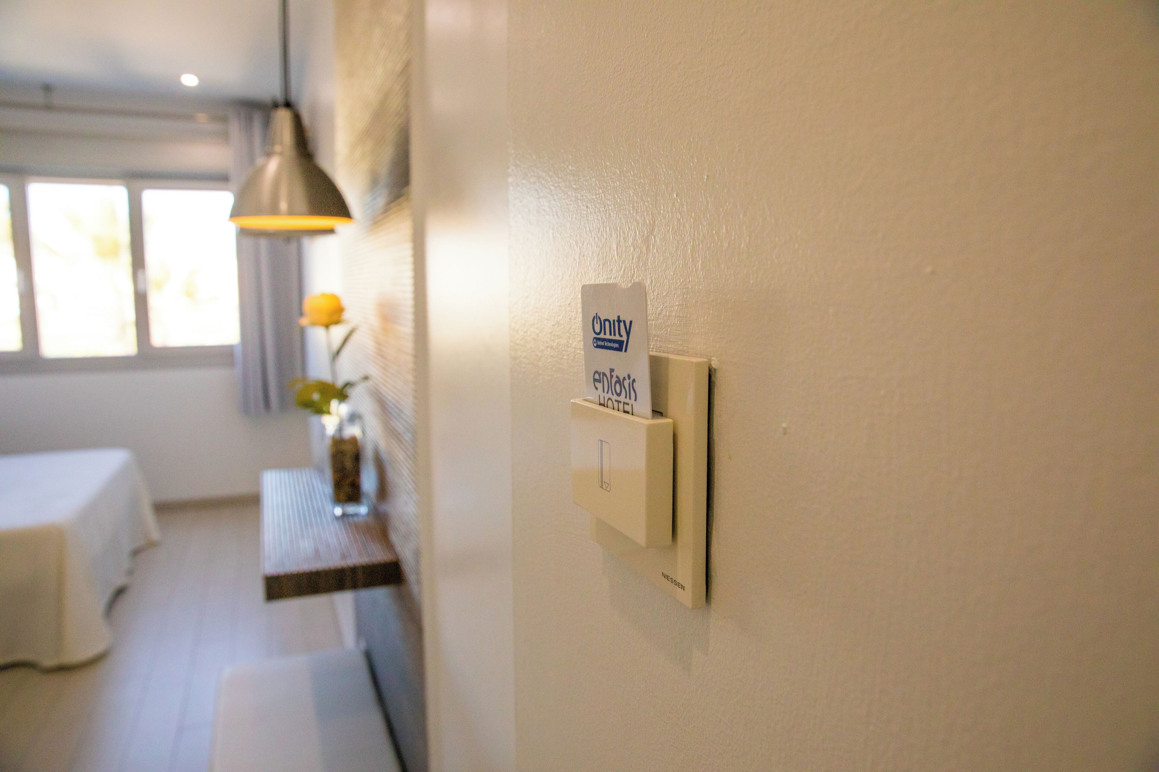 Una habitación de hotel con una cama, una mesita de noche con un florero y una lámpara fijada a la pared.