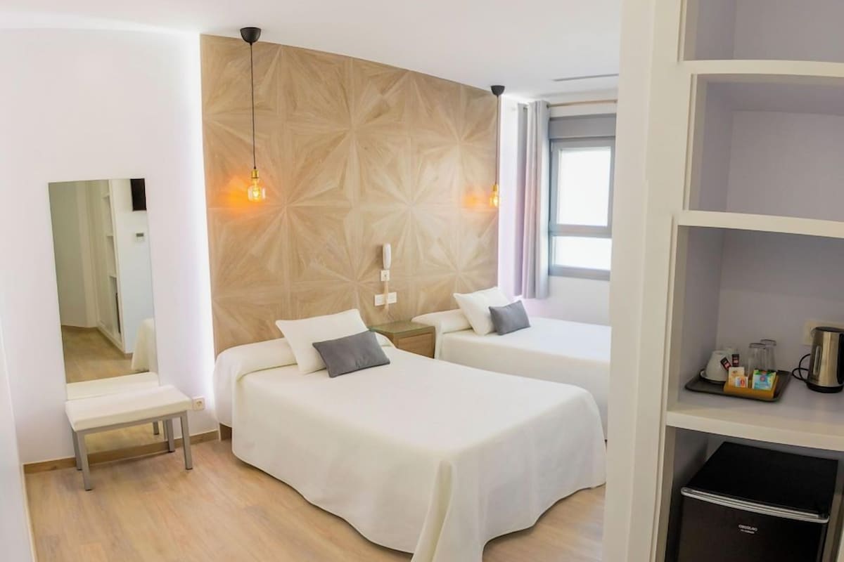 Hotellihuone, jossa on kaksi sänkyä, puinen korosteseinä, pieni pöytä ja sisäänrakennettu vaatekaappi.