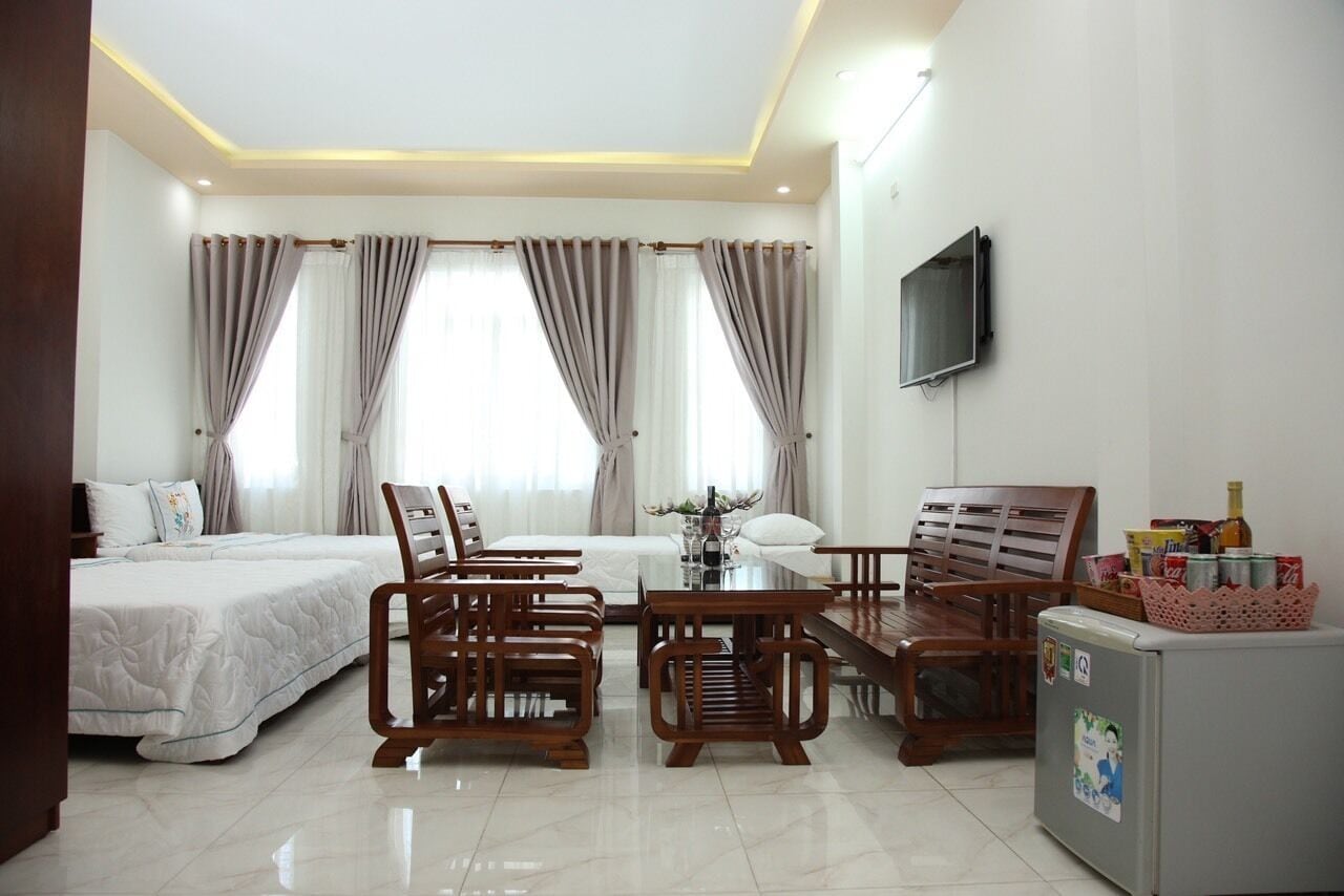 A hotel room with a bed, two wooden chairs, a small table, a TV, and a refrigerator.
