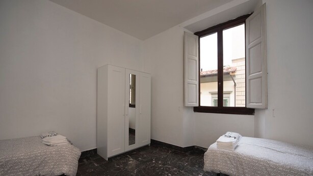 Ein Zimmer mit zwei Einzelbetten, einem Kleiderschrank und einem Fenster mit Fensterläden.