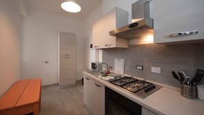 Eine moderne Küche mit Gaskochfeld, Spüle und Arbeitsplatte mit Küchenutensilien. Im Hintergrund ist eine Holzbank und eine Tür zu sehen.