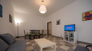 Ein Wohnzimmer mit Schachbrettmuster-Boden, einer Couch, einem Couchtisch, einem Fernseher auf einem Schrank und einem Essbereich mit Stühlen und einem Tisch.