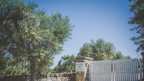 A gated entrance with a stone wall and a wooden fence, surrounded by trees. - Casa Ziazì (Monopoli)
