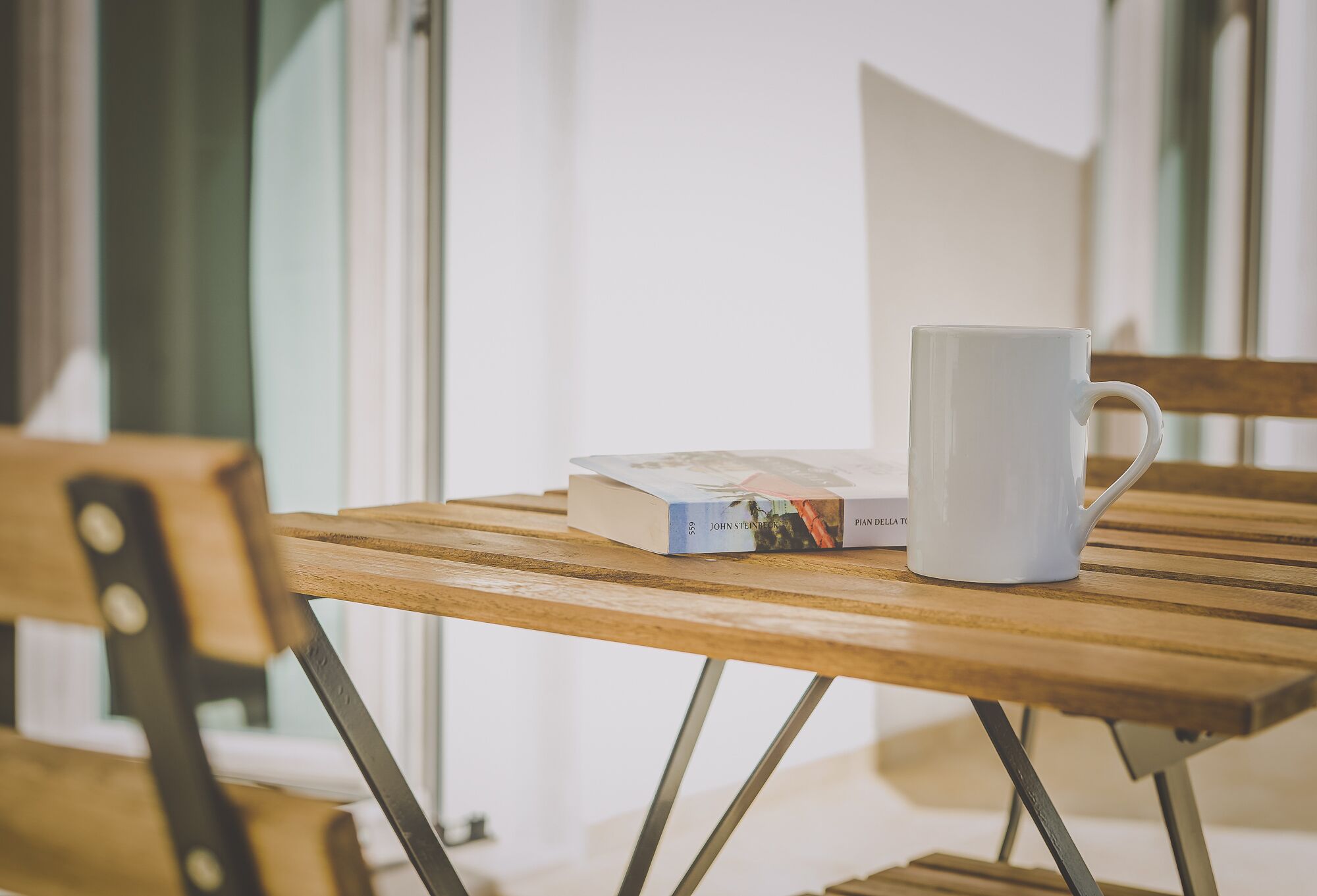 A wooden table with a white mug and a book titled "John Steinbeck" and "Pian della".