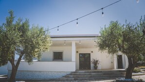 A house with a white exterior, a black door, and a small window. There are two trees in front of the house. - Casa Ziazì (Monopoli)