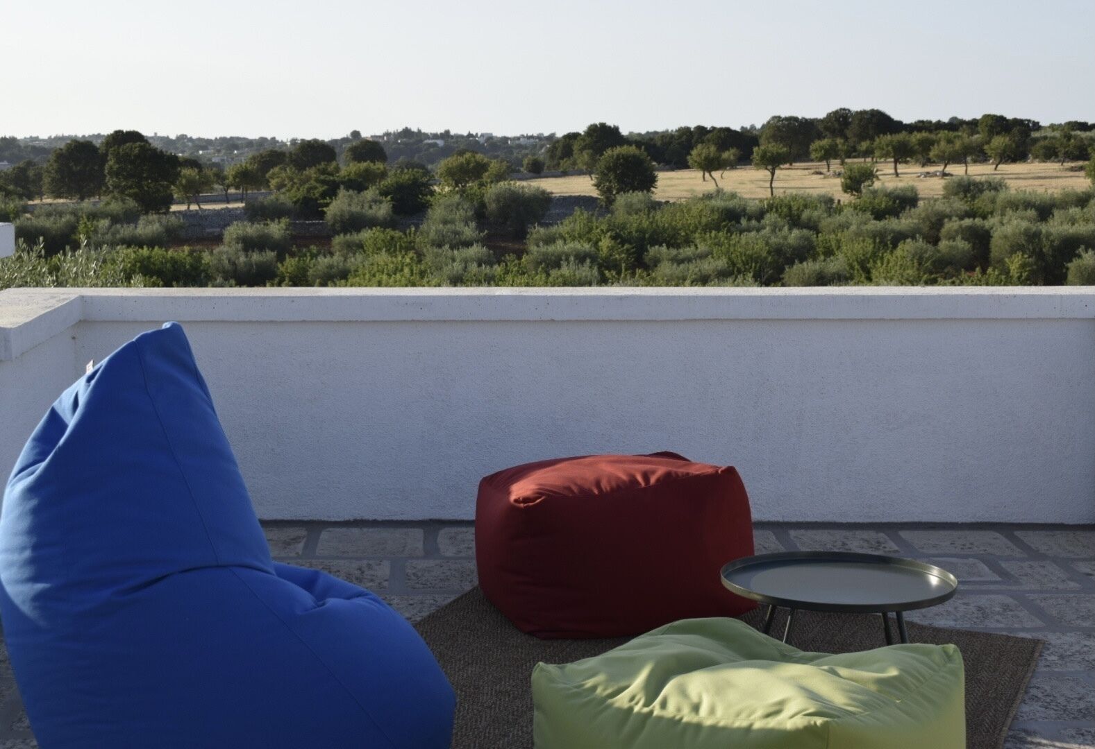 Une terrasse sur le toit offrant une vue sur un paysage rural, avec un pouf rouge, un pouf bleu et une petite table ronde.