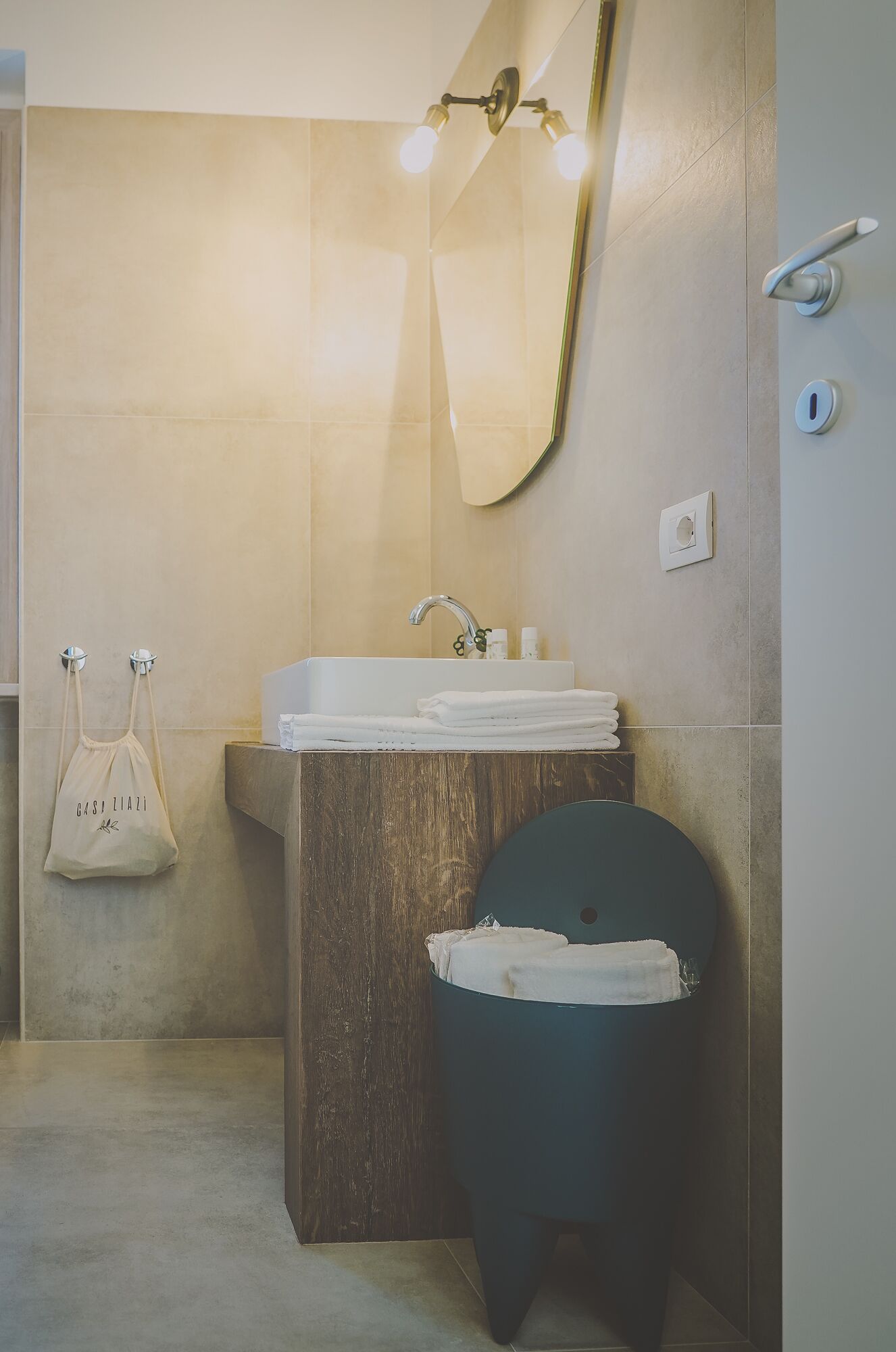 A bathroom with a wooden vanity, a sink, and a toilet. There is a towel rack with a white towel and a white bag hanging on it.